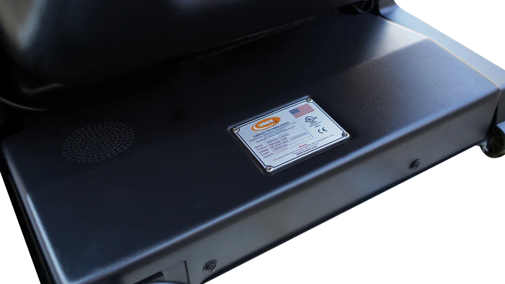 Close-up of the underside of a black grill or appliance, showing a metal铭牌 label with regulatory text and a circular vent on the left.